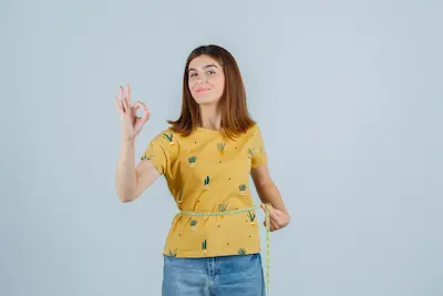 Mujer midiendo su cintura con cinta métrica y sonriendo